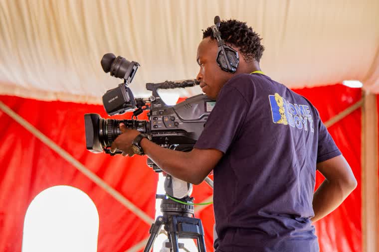 Camera operator in profile against a red stage backdrop
