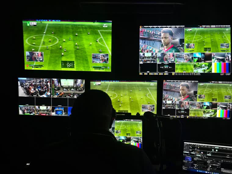 Vision operator silhouetted against a wall of live esports match feeds
