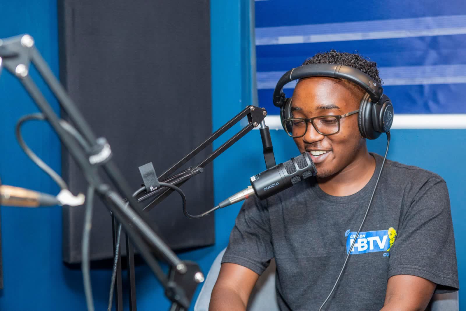 Presenter laughing at a studio microphone wearing an HBTV shirt