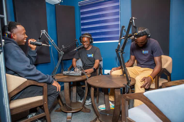 Three presenters around microphones in the HBTV studio