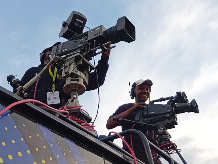 Two camera operators on a riser against open sky
